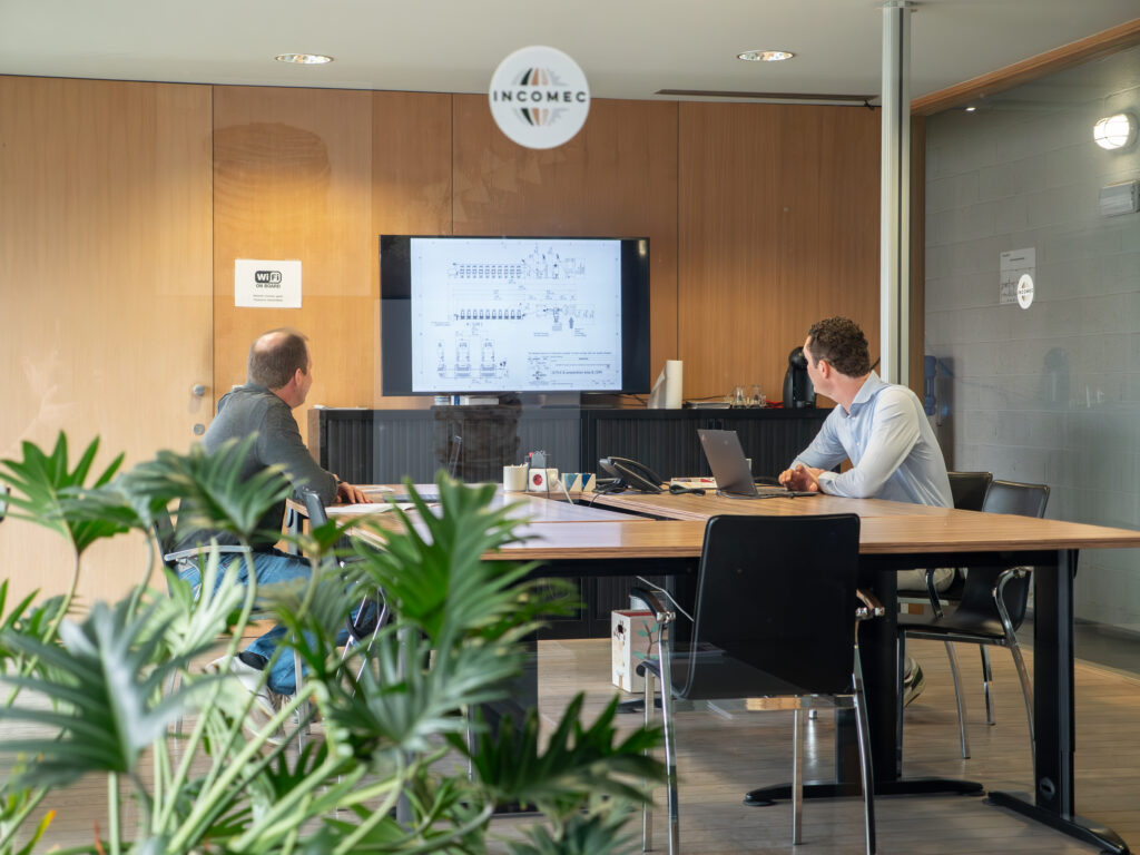 Twee Incomec-medewerkers bespreken een technisch ontwerp van een industriële productielijn in de vergaderruimte.