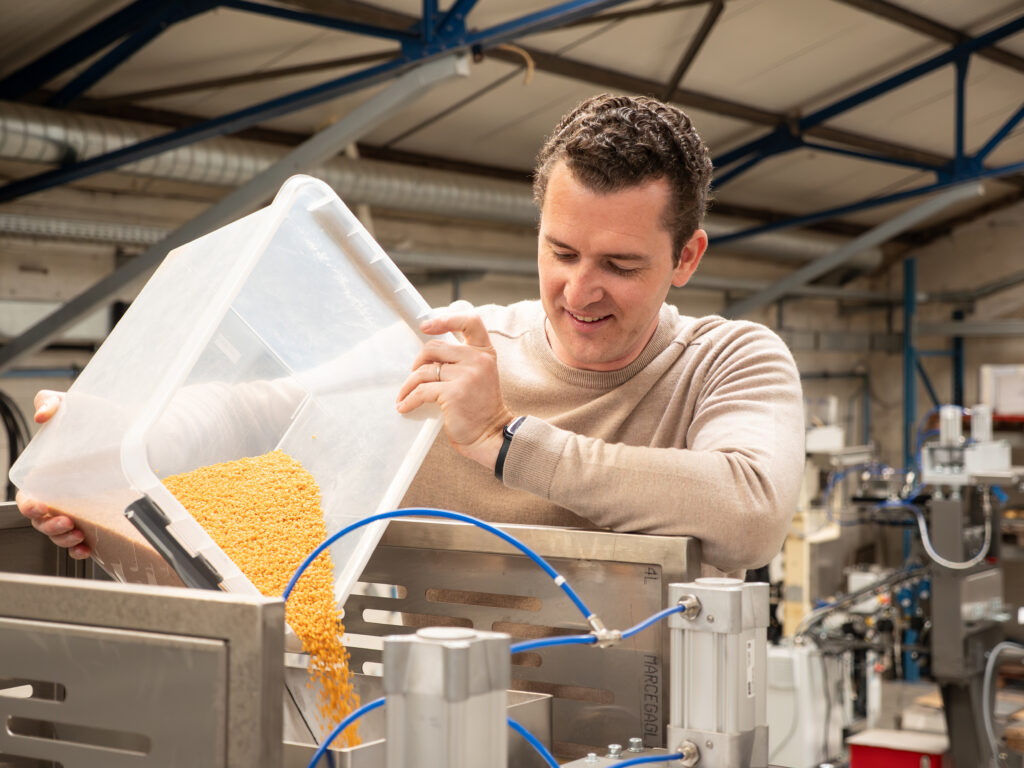 Medewerker vult een industriële snackmachine met maïskorrels voor de productie van gepofte snacks.
