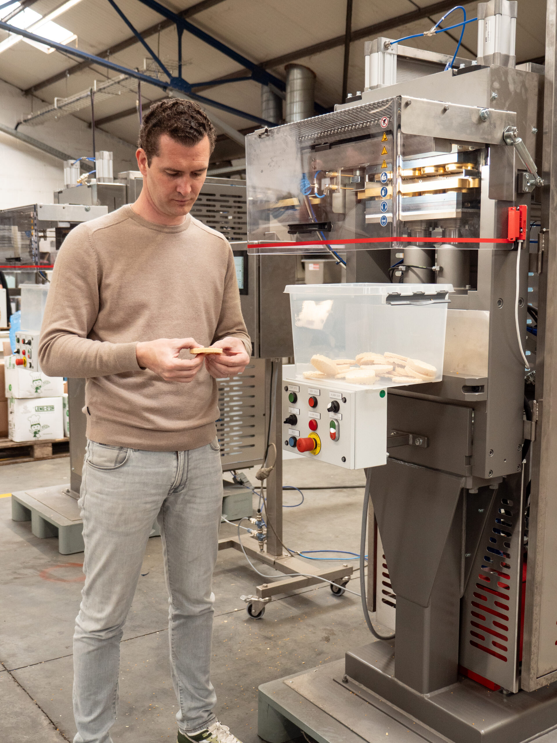 Medewerker controleert een gepofte snack naast een industriële machine voor snackproductie.