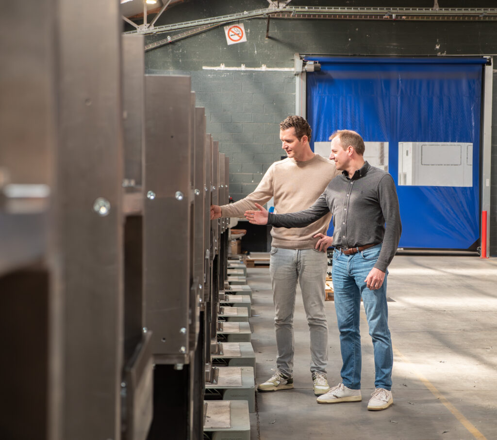 Twee Incomec-medewerkers bespreken een rij industriële machines voor de productie van gepofte snacks.