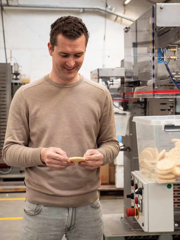 Medewerker controleert een gepofte snack naast een industriële machine voor snackproductie.